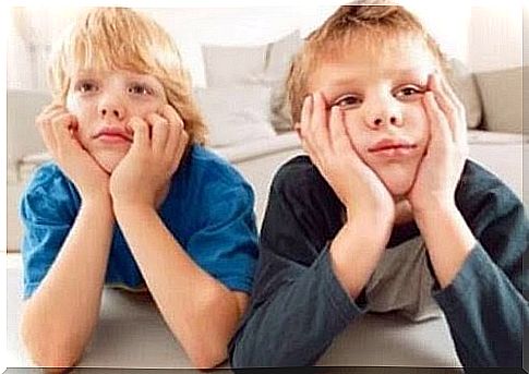 Two children are lying on the floor watching TV