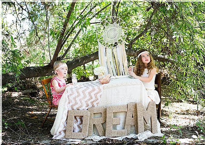 two girls are sitting at a table with the word "DREAM" on and a dream catcher is hanging above them