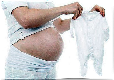 Pregnant woman holding up baby clothes