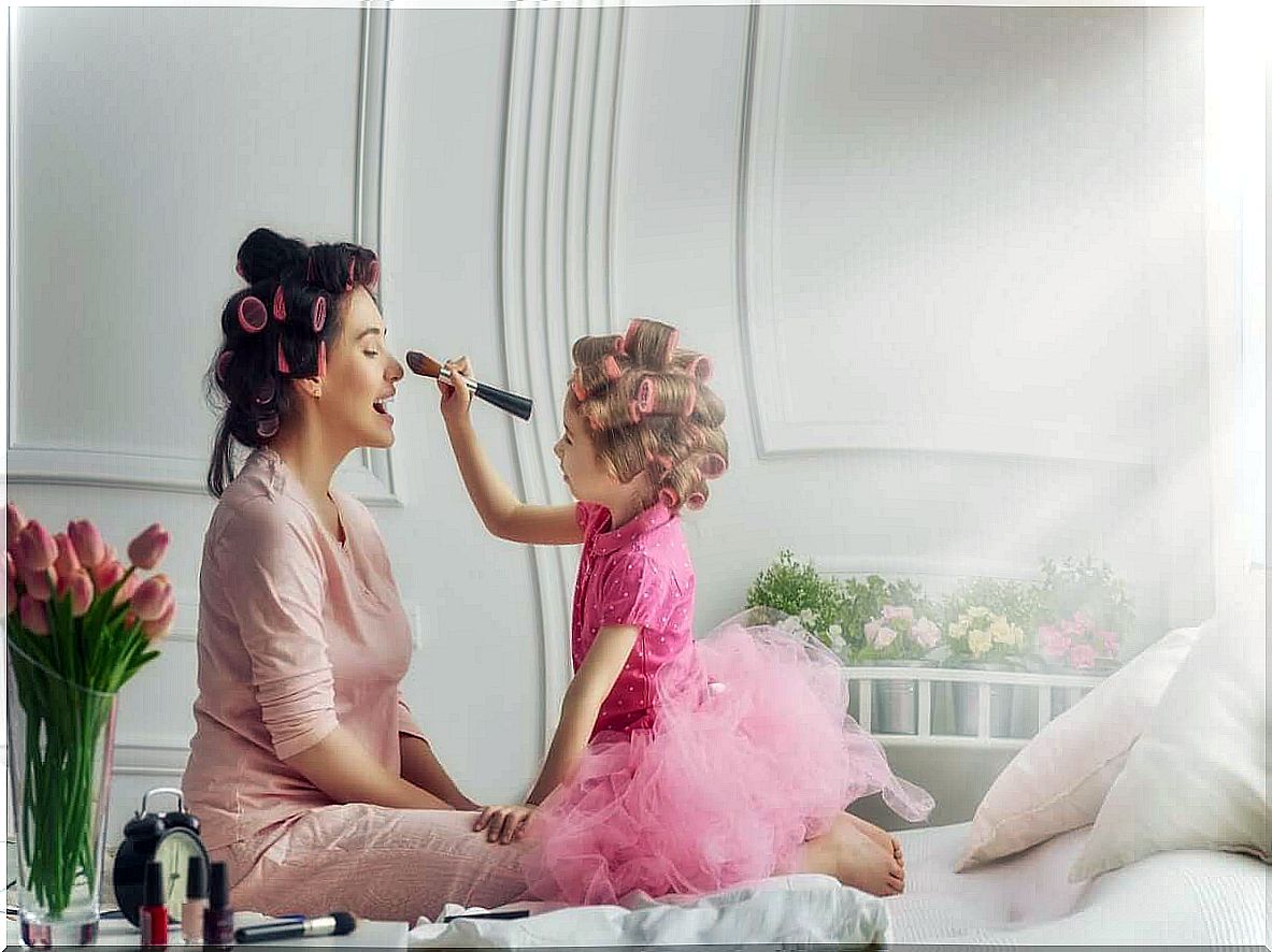 A daughter who puts make-up on her mother's face while they both wear curlers in their hair.