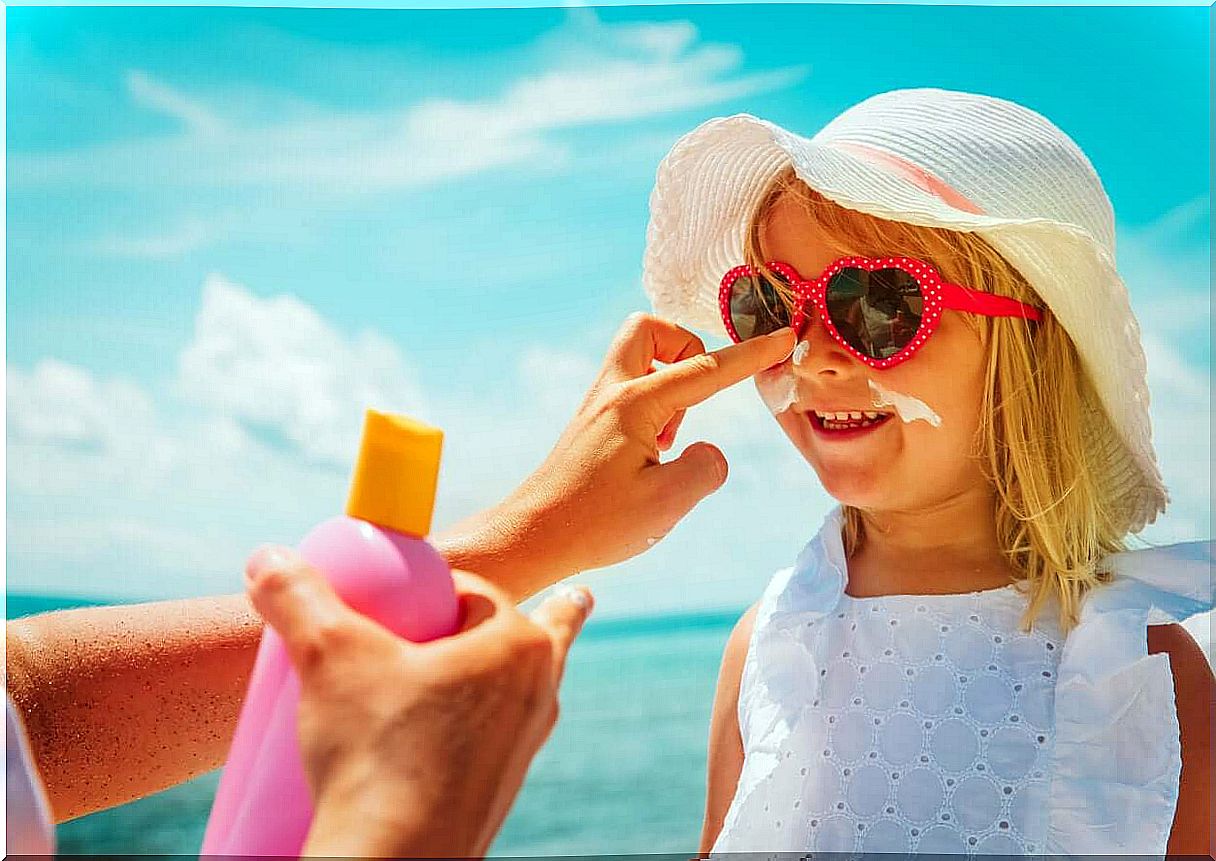 A mother applying sunscreen to her daughter's face on the beach.