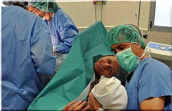 new mother at operating table greets her newborn baby, father is sitting with